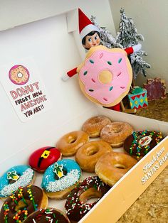 a box filled with lots of donuts on top of a counter next to a christmas tree