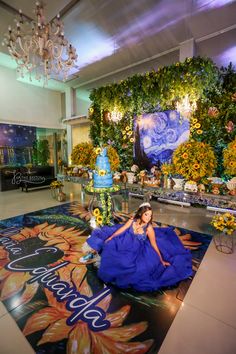 a woman in a blue dress sitting on the floor next to a cake and flowers