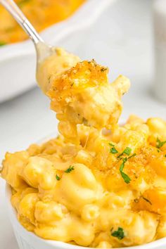 a spoon full of macaroni and cheese is being lifted from a white bowl