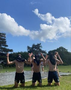 three boys are standing in the grass with their arms up and one boy is holding his head