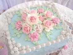 a blue and white cake with pink flowers on the top is sitting on a doily