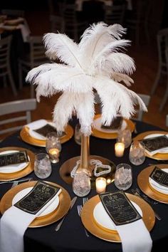 there is a table set with gold and white plates, place settings and a palm tree centerpiece