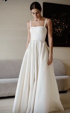 a woman in a white dress is standing near a couch and looking down at the floor