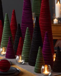 there are many small christmas trees on the table with candles in front of each one