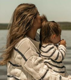 a woman holding a small child in her arms by the water's edge,