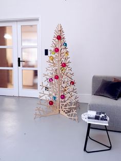 a wooden christmas tree sitting next to a couch in a living room with white walls