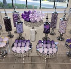 purple and white candies are displayed in glass bowls on a table with silver candlesticks