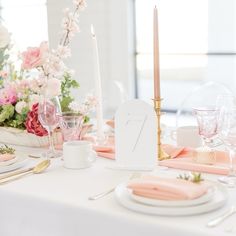 the table is set with pink and white plates, silverware, candles and flowers