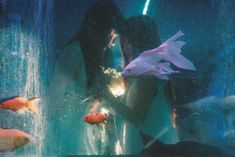 two women are looking at fish in an aquarium with water spraying from the bottom and one woman is holding her hand out