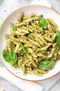 a white bowl filled with pesto pasta on top of a table next to a fork