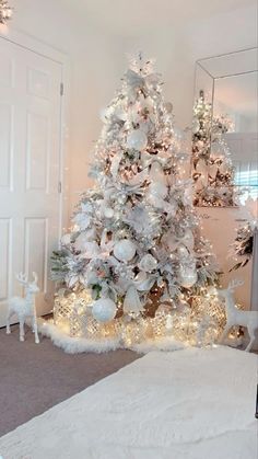 a white christmas tree with silver ornaments and lights in a room next to a mirror