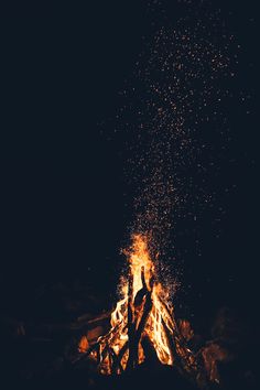 two people standing in front of a campfire with lots of fire and sparks coming out of it