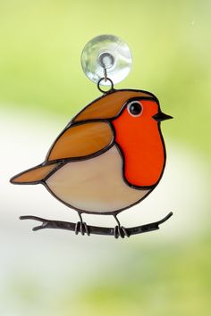 a stained glass bird ornament hanging on a branch with a light bulb in the background