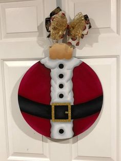 a santa clause ornament hanging on the front door with gold ribbon and bows