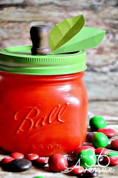 a red mason jar filled with candy and green leaf