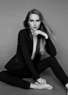 a woman sitting on the ground with her legs crossed and wearing black clothing, posing in front of a gray background