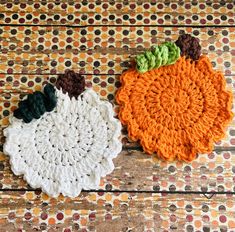 two crocheted pumpkin coasters sitting on top of a wooden table next to each other