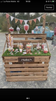 a wooden box filled with lots of candy on top of a gravel ground next to a blue car