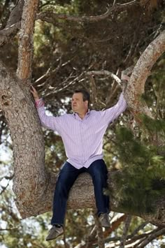 a man sitting on top of a tree branch with his arms out in the air