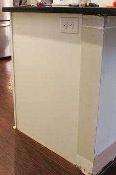 a kitchen island with black counter top and wooden flooring in front of the refrigerator