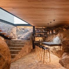 an indoor bar with stone walls and steps leading up to the top floor, along with several stools