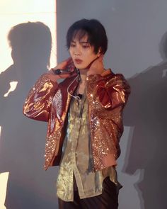 a young man wearing a gold jacket and black pants standing in front of a wall