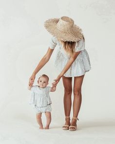 a woman holding the hand of a small child wearing a straw hat and white dress