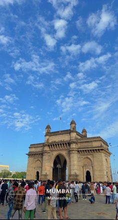 many people are walking around in front of a large building under a blue sky with white clouds