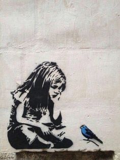 a blue bird sitting on the ground next to a wall with a drawing of a woman