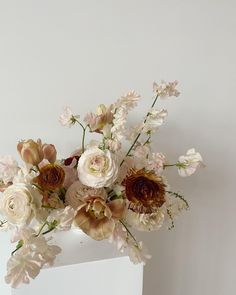 an arrangement of flowers in a vase on a white shelf against a plain wall background