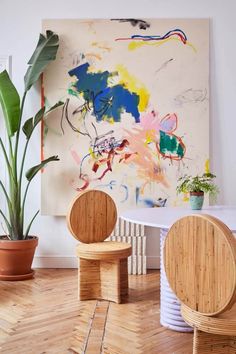 two wooden chairs sitting in front of a painting on the wall next to a potted plant