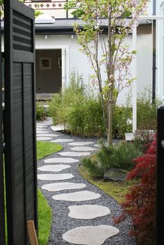 a garden with stepping stones and trees in the background, leading to a white house