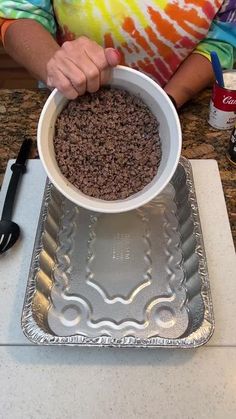 a person holding a bowl over a metal pan on top of a counter with food in it