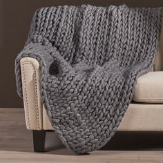 a gray knitted blanket sitting on top of a couch next to a white chair