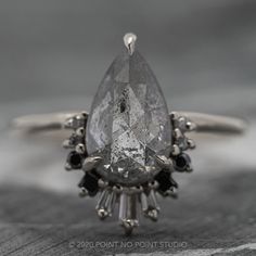 a close up view of an engagement ring with a pear shaped diamond surrounded by black diamonds