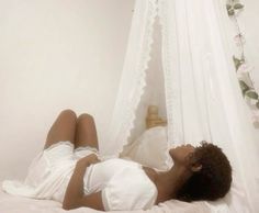 a woman laying on top of a bed next to a white curtain