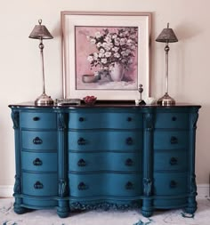 a blue dresser with two lamps and a painting on the wall behind it in a living room