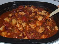 a person holding a wooden spoon in a crock pot filled with stew and meat