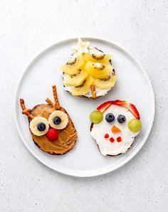 a white plate topped with two sandwiches covered in fruit and an owl face made out of kiwis