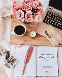 a desk with a laptop, notebook and flowers on it next to a cup of coffee