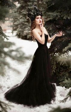 a woman in a long black dress is standing in the snow with her hand on her face