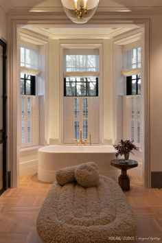 a bath tub sitting under two windows next to a table with pillows on top of it