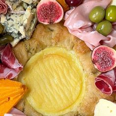 an assortment of meats and cheeses on a platter with orange slices, grapes, olives, and bread