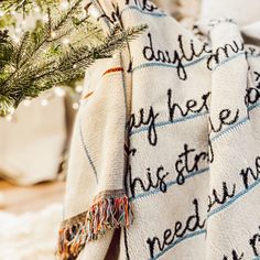 a white blanket with words written on it next to a small christmas tree in a potted plant