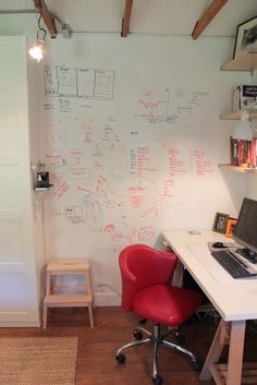 a desk with a laptop computer on top of it next to a red chair and bookshelf