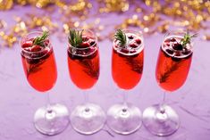 three wine glasses filled with red liquid and garnished with greenery, sitting on a purple surface