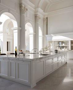 a large white kitchen with an island in the middle and columns on both sides, along with marble flooring