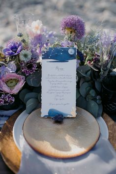 a table setting with flowers and a menu card on top of the plate, surrounded by greenery