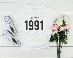 a white t - shirt with the year 1911 printed on it next to some flowers