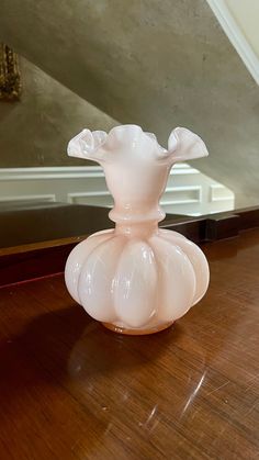 a pink glass vase sitting on top of a wooden table in front of a mirror